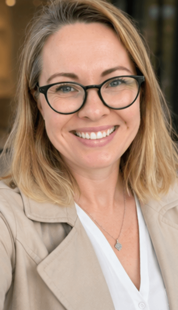 Frau mit blonden Haaren und Brille, die lächelt und verschränkte Arme hat.